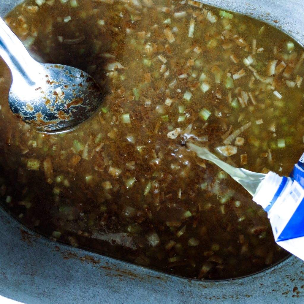 Chicken broth poured into a pot of Chicken Gumbo, Simply Classic Cajun.