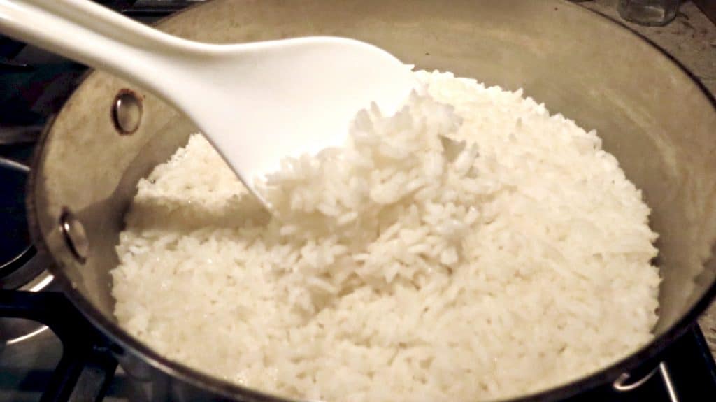 A pot of white rice with a white spoon scooping rice up.