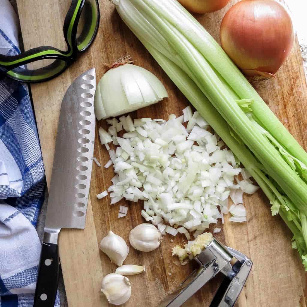 Onions, celery, garlic, and knife on wooden cutting board for Chicken Gumbo, Simply Classic Cajun.