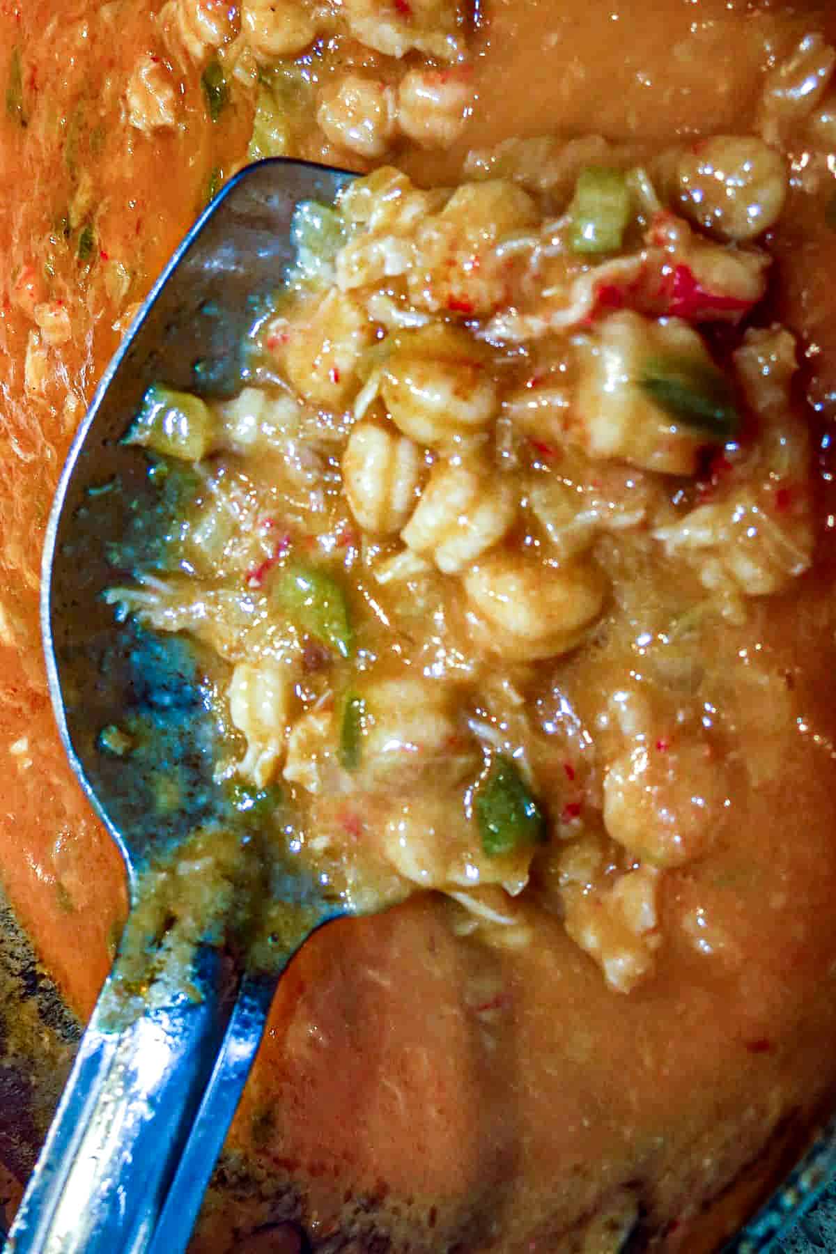 A long-handled silver spoon in a pot of stew with a scoop of crawfish in gravy.