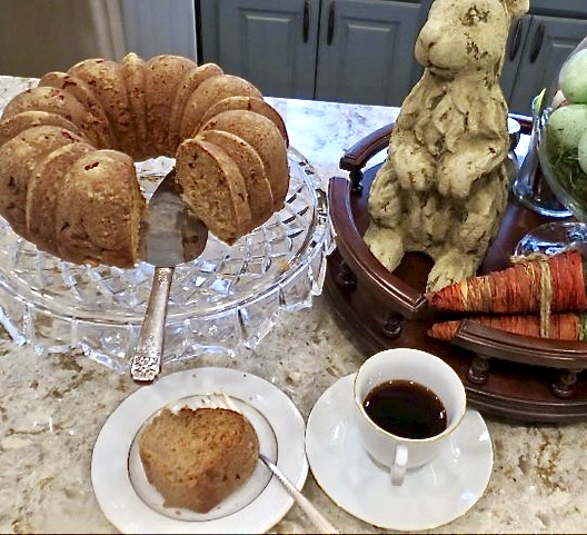 MaMa's Fresh Apple Cake on a glass cake stand with a piece of cake on a white plat on the side.