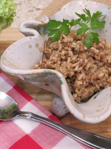 Rice dressing in a serving dish with red checkered napkin and spoon.