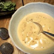 A spoon in a blue bowl of seafood bisque with lumps of crab and shrimp. on a wooden table with small salt and pepper shakers.