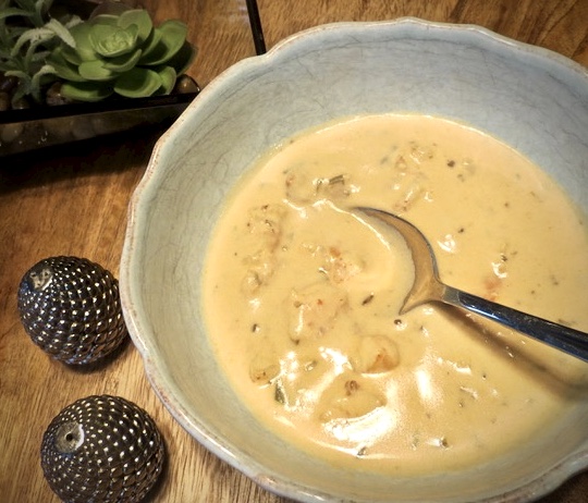 A spoon in a blue bowl of seafood bisque with lumps of crab and shrimp. on a wooden table with small salt and pepper shakers.