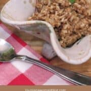 Rice dressing in a white pottery dish with a silver serving spoon on a red and white checked napkin.