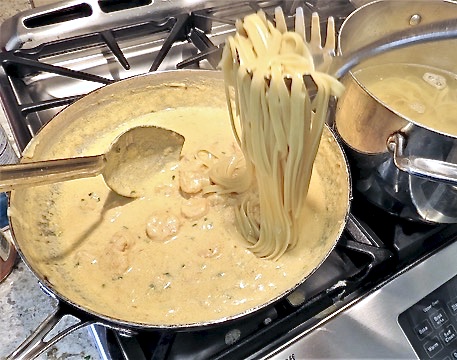 Pasta spooned into a pot of sauce.