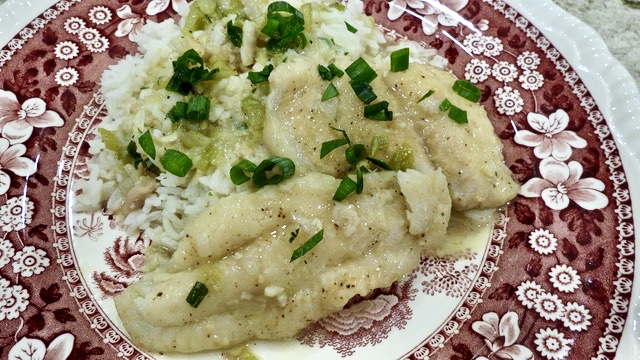 A serving of Fish Court-Bouillon over a bed of rice on a red and white toille plate.