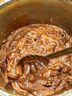A spoon stirring pecans in pralines.