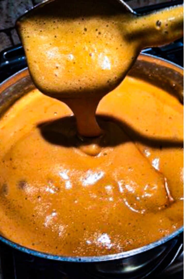 A spoon pouring praline sauce into a pot of the sauce.