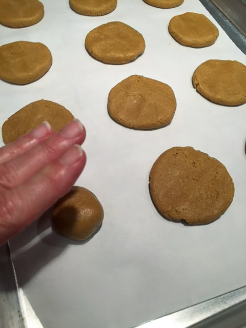 Hand pressing balls of cookie dough into disks.