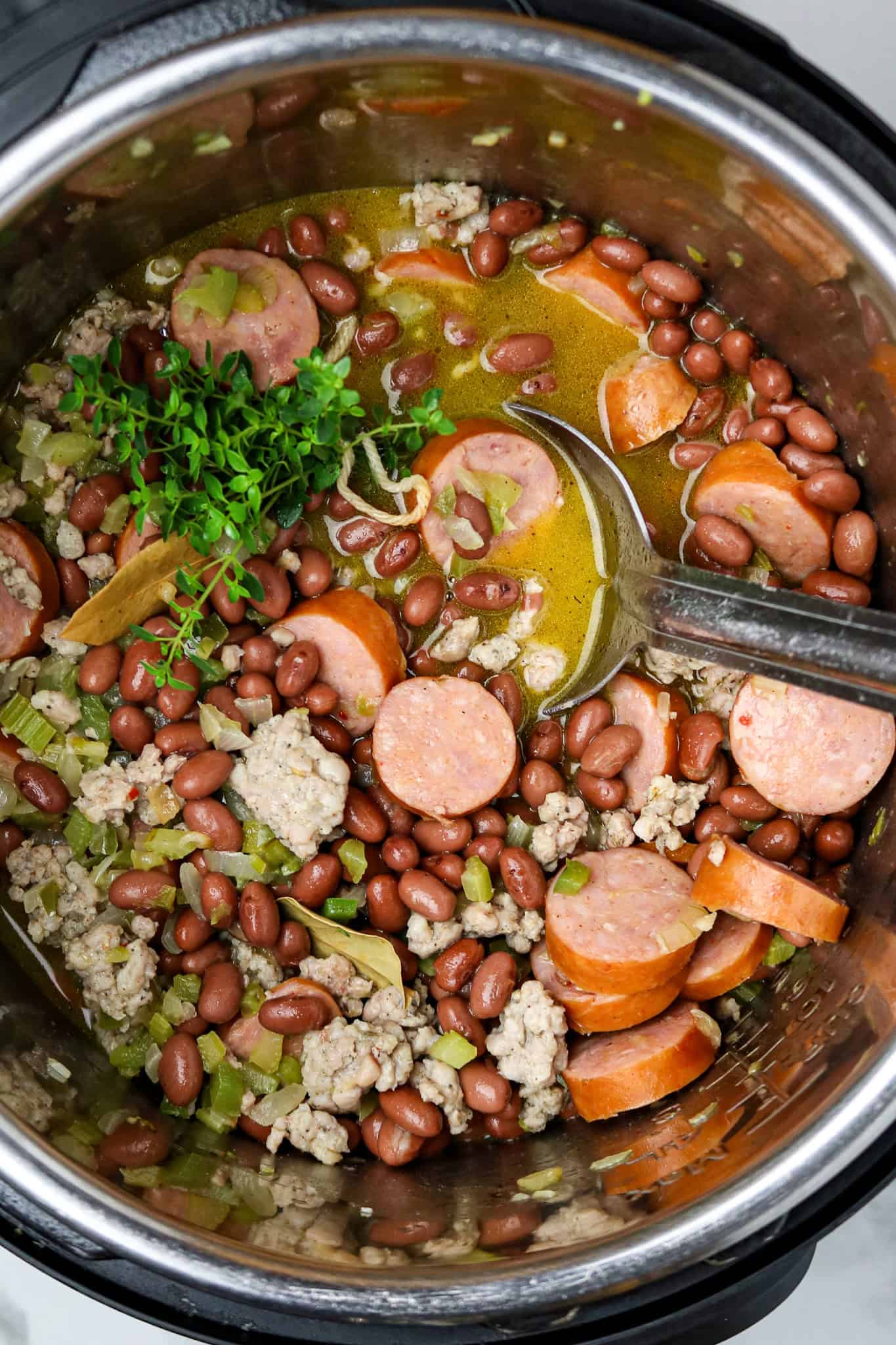 A long-handled silver spoon stirring beans and sausage in a pot.