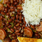 A plate of red beans with sausage and rice with a scoop of white rice and a wedge of corn bread on a white plate.