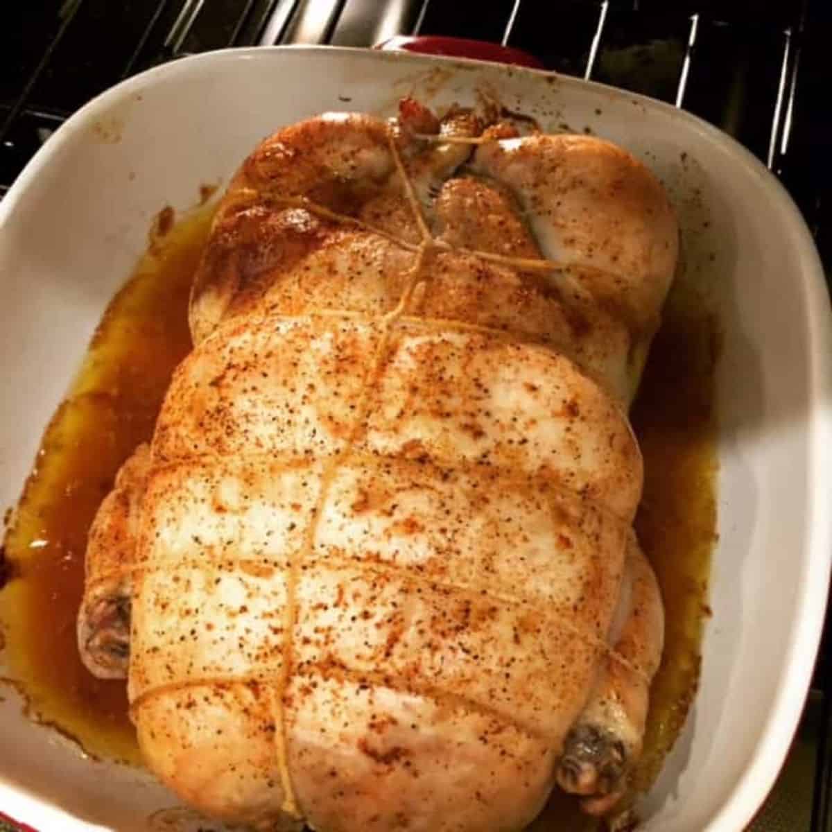 A baked whiole chicken tied up with butcher's twine in a white roasting pan.