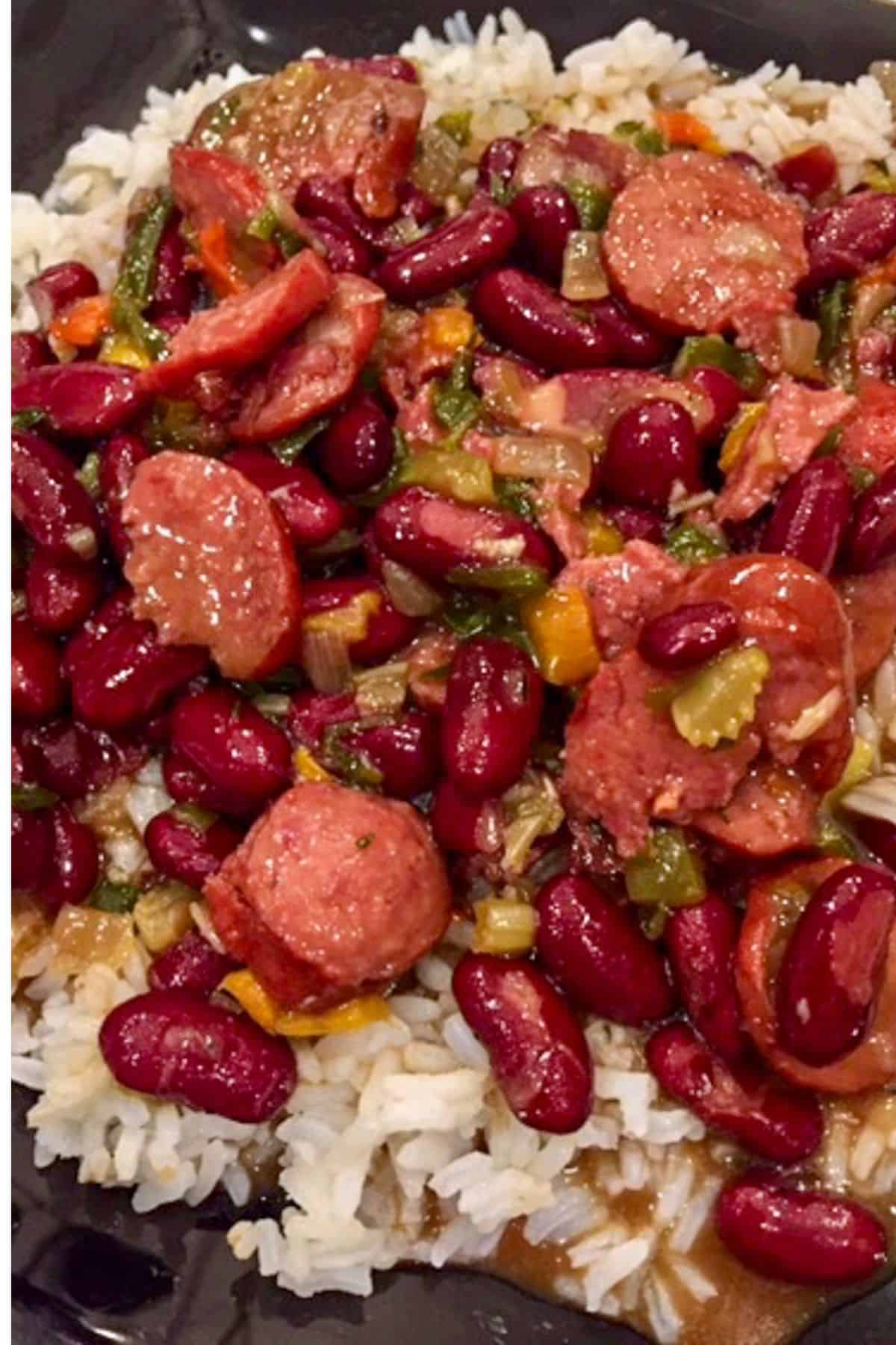A plate of red beans with sausage and rice on a mound of white rice.