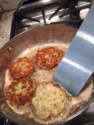 A pan of fish cakes being turned with a spatula.