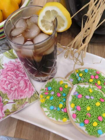 A glass of iced drink with lemon slice and sugar cookies.