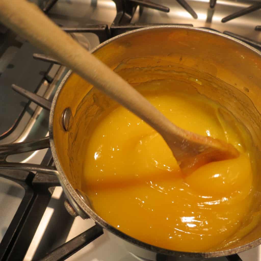 A pot of lemon yellow sauce stirred with a wooden spoon.