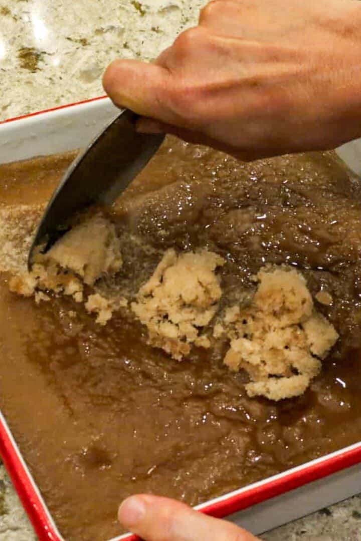 A square dish of frozen root beer and a hand scraping a spoon across it to make slush.