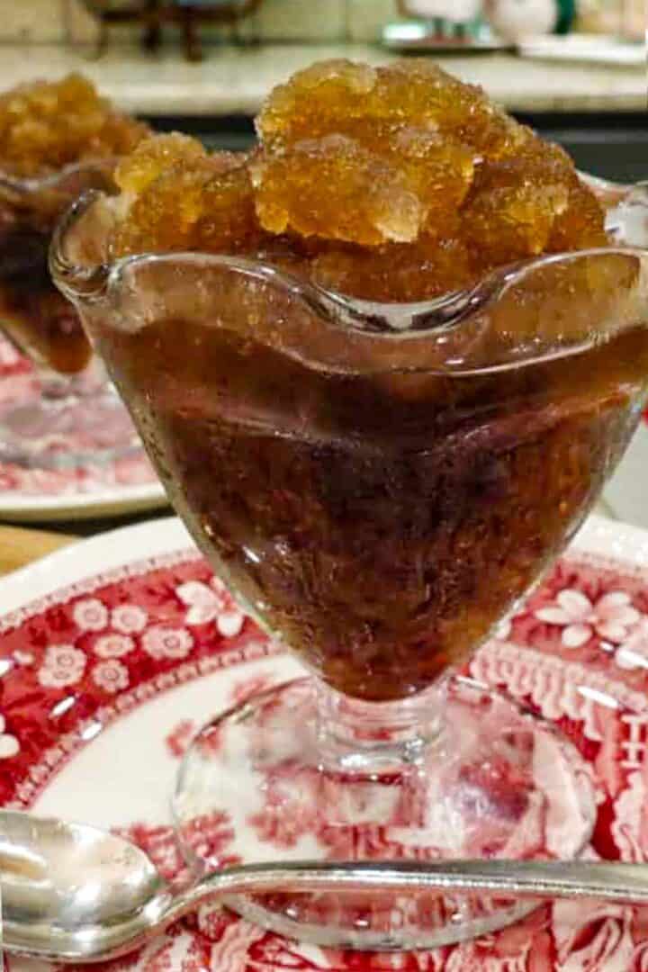 A footed glass dessert cup with root beer shush in it.