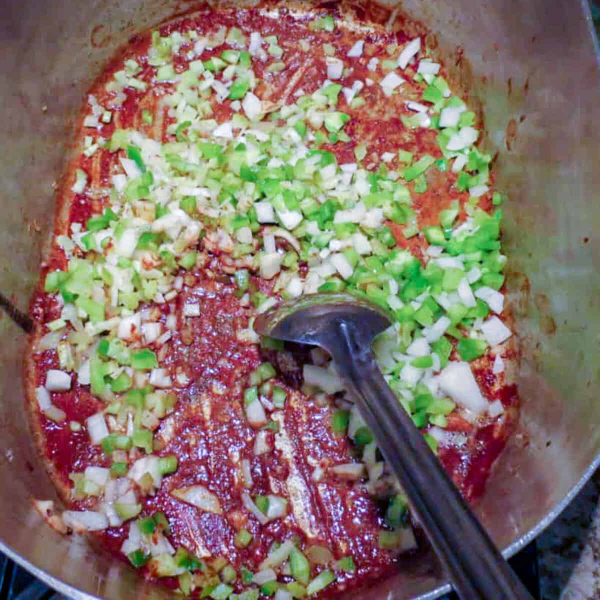A pot with roux and the Cajun trinity of chopped vegetables and a spoon in it for chicken fricassee.
