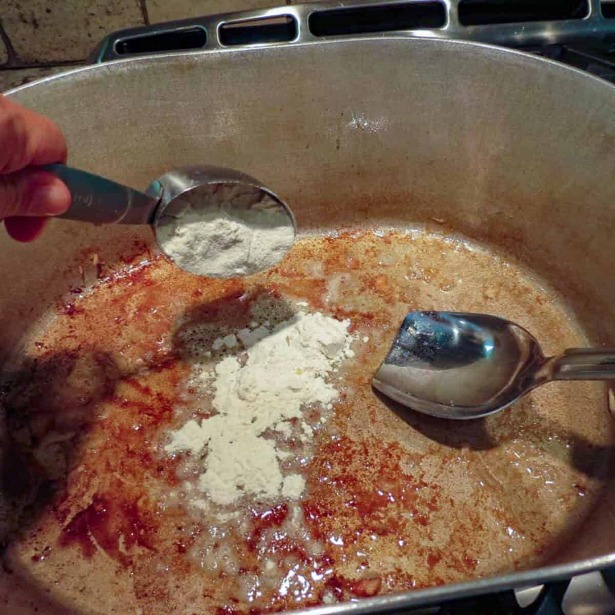 A person stirring a pot of flour and oil with a spoon.