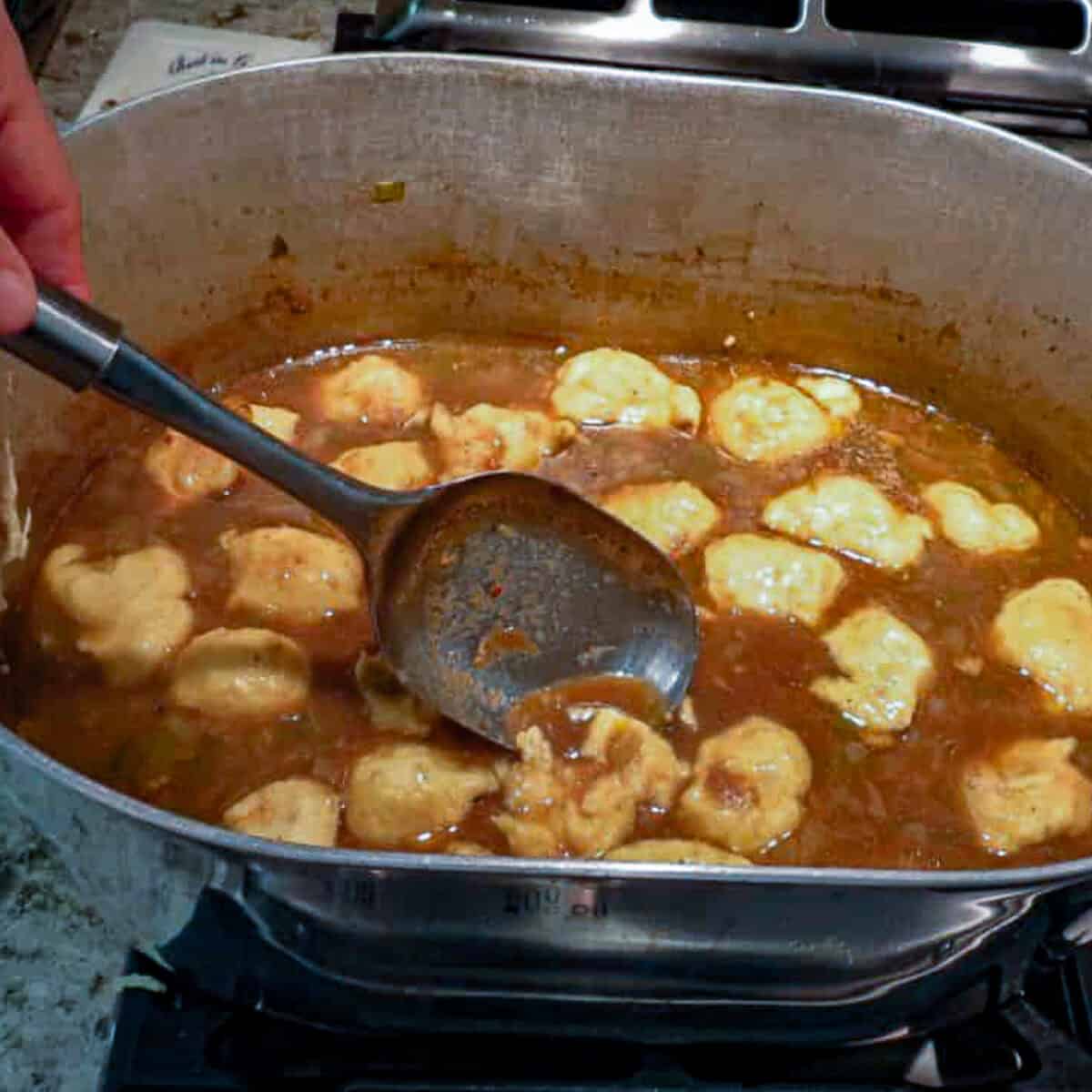 A person stirring up some chicken fricassee with dumplings in a pot.