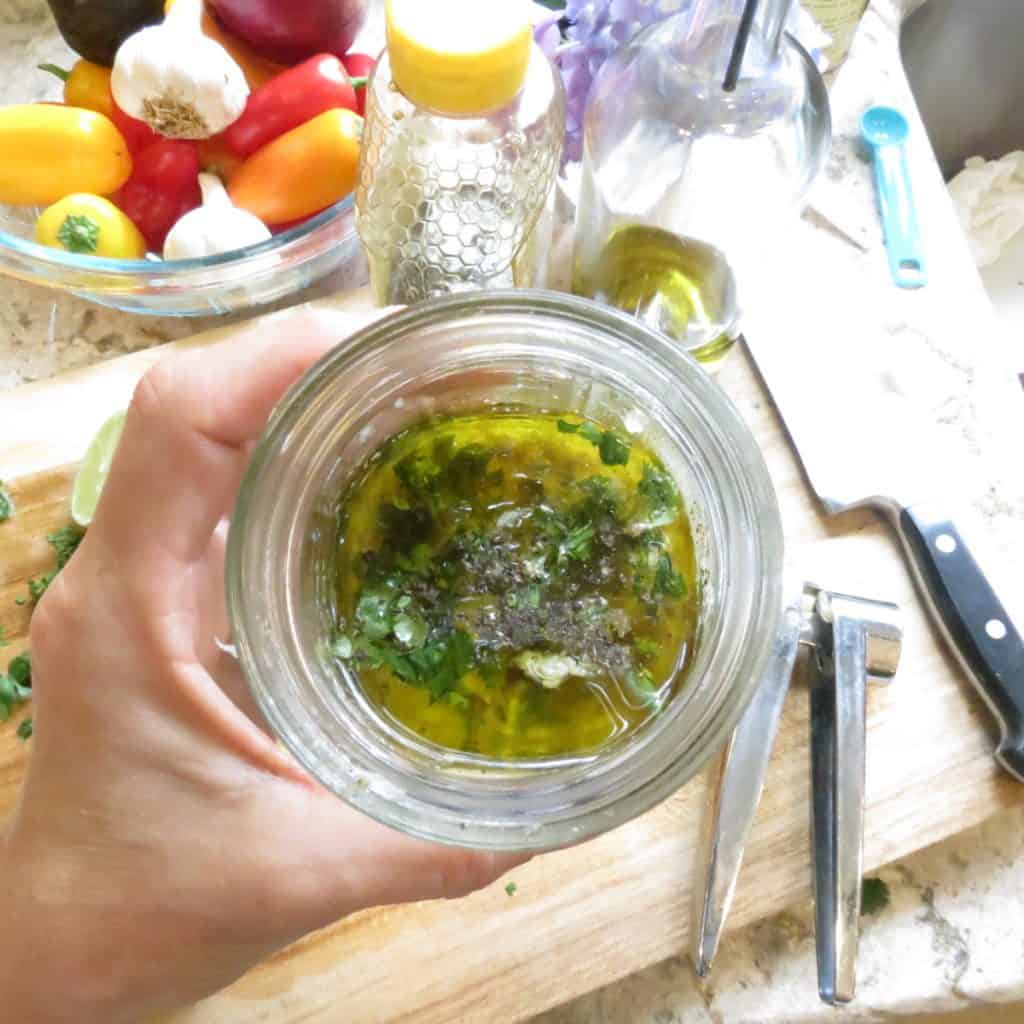 A hand holding a jar of vinaigrette dressing.