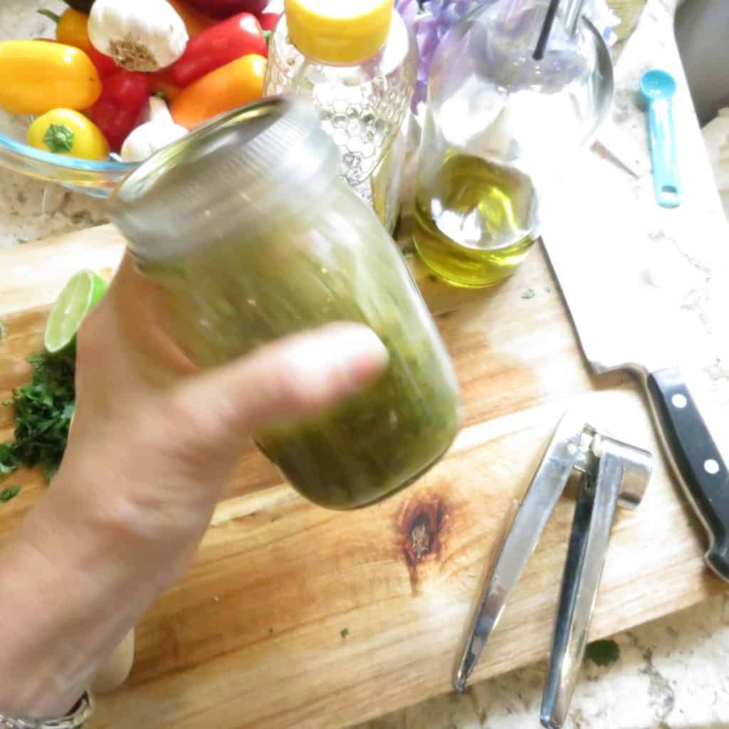 A hand shaking a jar of vinaigrette with a bowl of peppers.