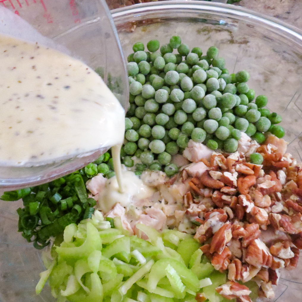 Lemon greek yogurt dressing poured onto ingredients for Chicken Salad With Green Peas in a glass bowl.