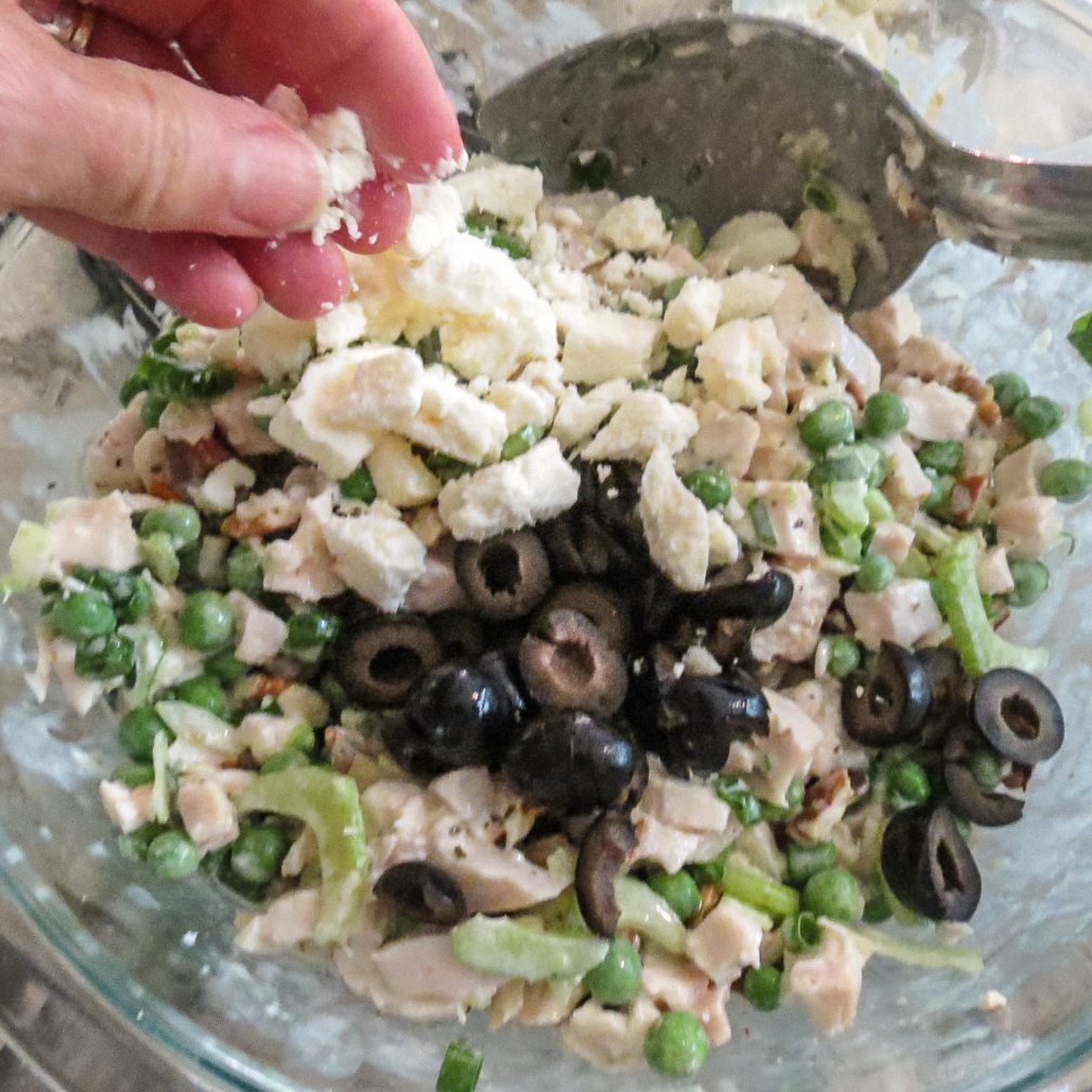 Ingredients of Chicken Salad With Green Peas in a bowl before they are tossed together with feta cheese sprinkled on top.