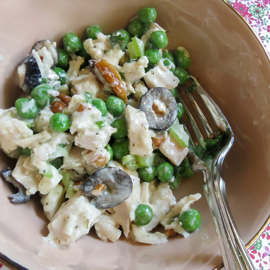 Chicken Salad With Green Peas in a pink bowl with a silver fork on a floral place mat.