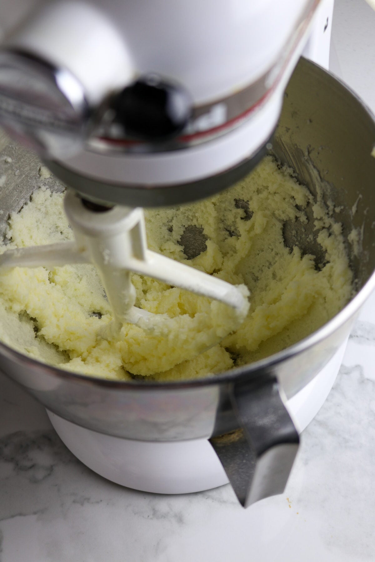 A silver bowl with kitchen aid mixer stirring butter an sugar in it.