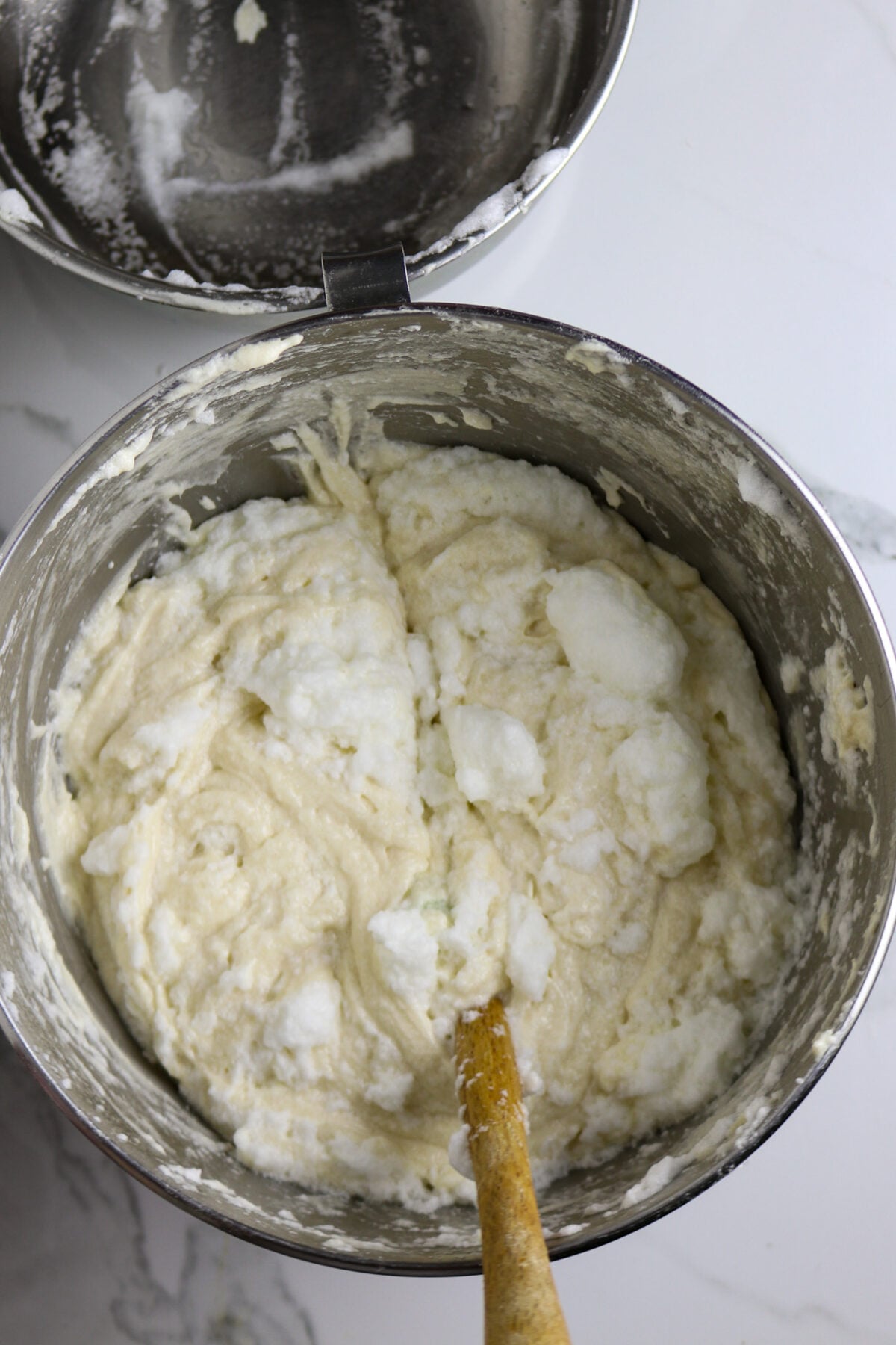 A spatula cutting through white cake mix incorporating beten egg whites in a liver bowl.