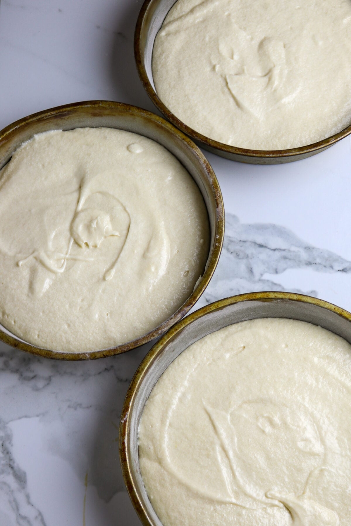 Three round cake pans with cake mix ready for the oven.