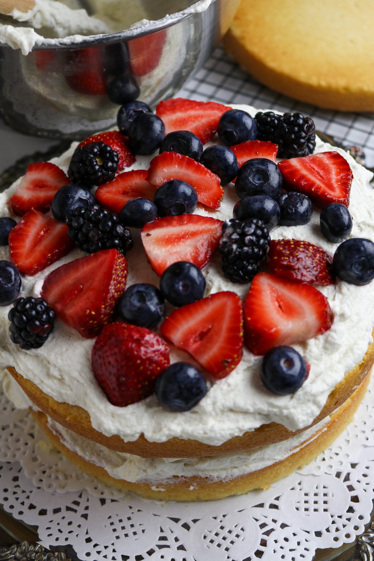 A white 2 layer cake with vanilla frosting and fresh berries on top.