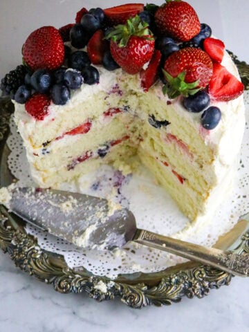 A white 3 layer cake with vanilla frosting and fresh berries on top.
