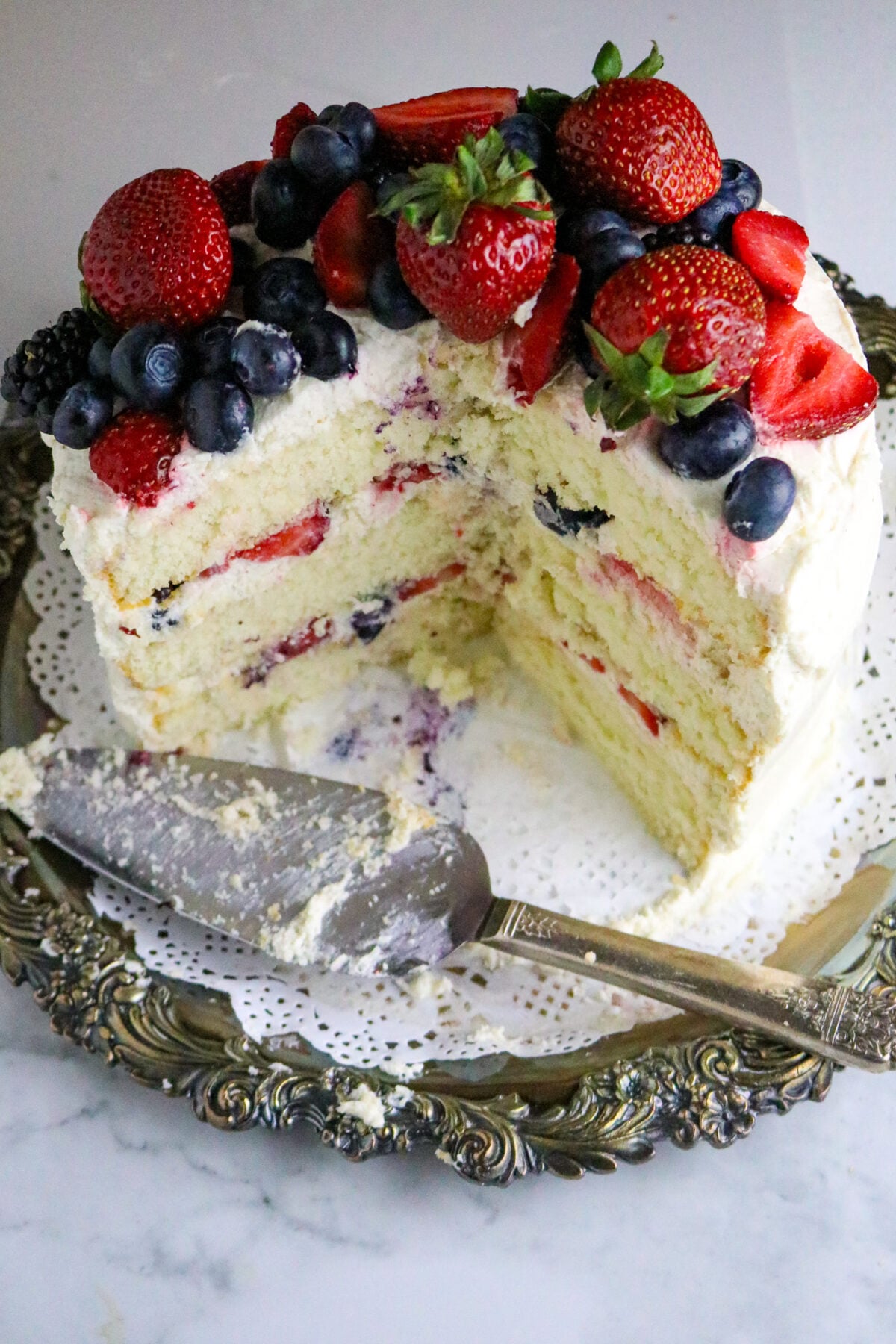 A white 3 layer cake with vanilla frosting and fresh berries on top.