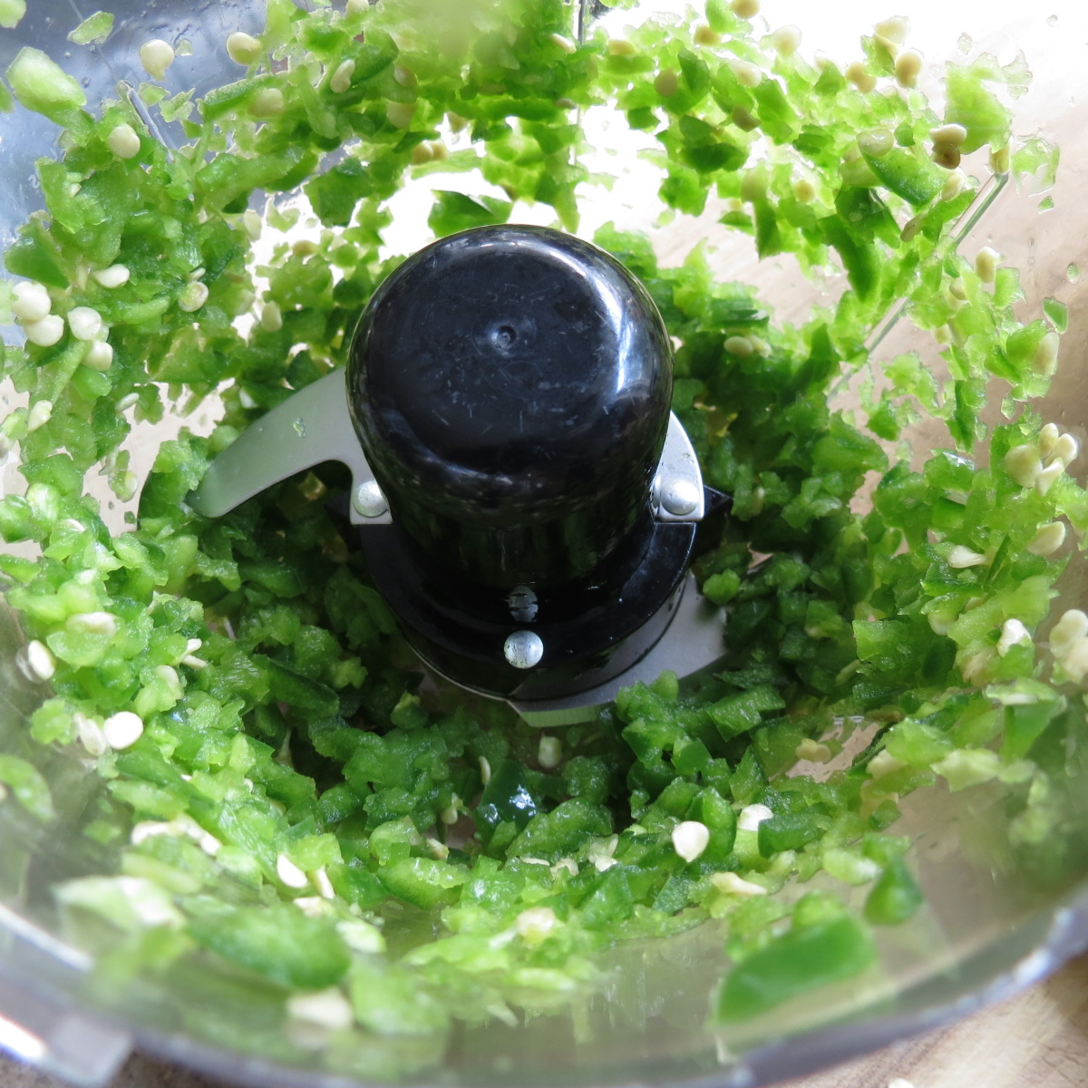 A food processer bowl with a blade and cut up green peppers.