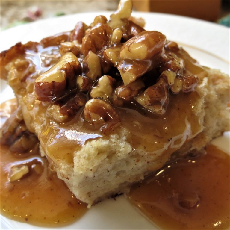 Bread Pudding topped with a Pumpkin Pecan Praline Sauce on white plate.