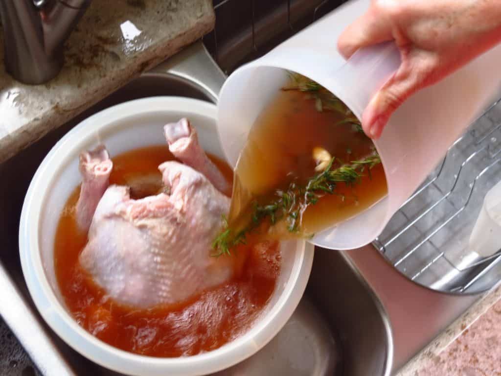 A turkey in a large container with a pitcher of Brine mixture poured over it.