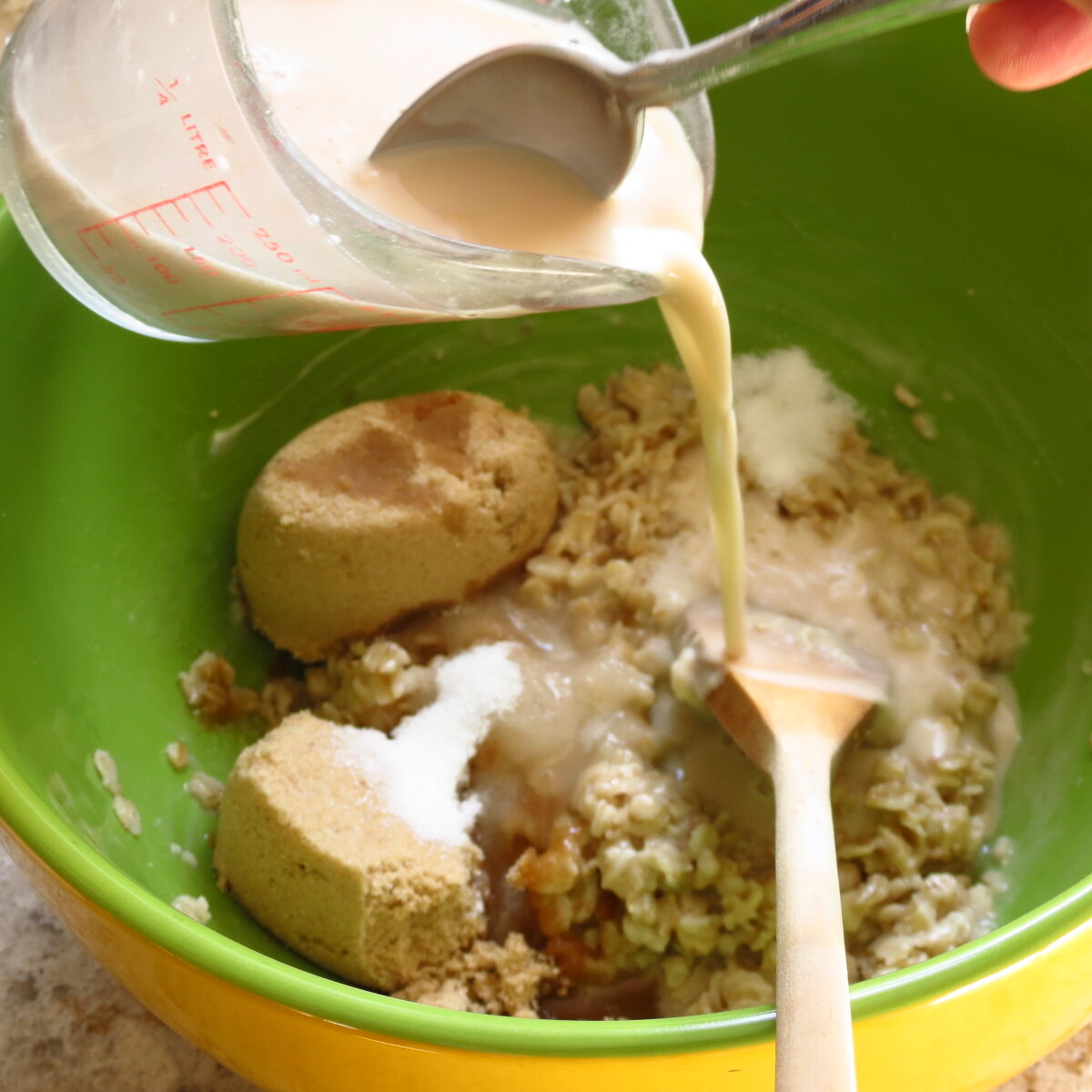 A cup of yeast and water mixture poured over a bowl of dry ingredients.