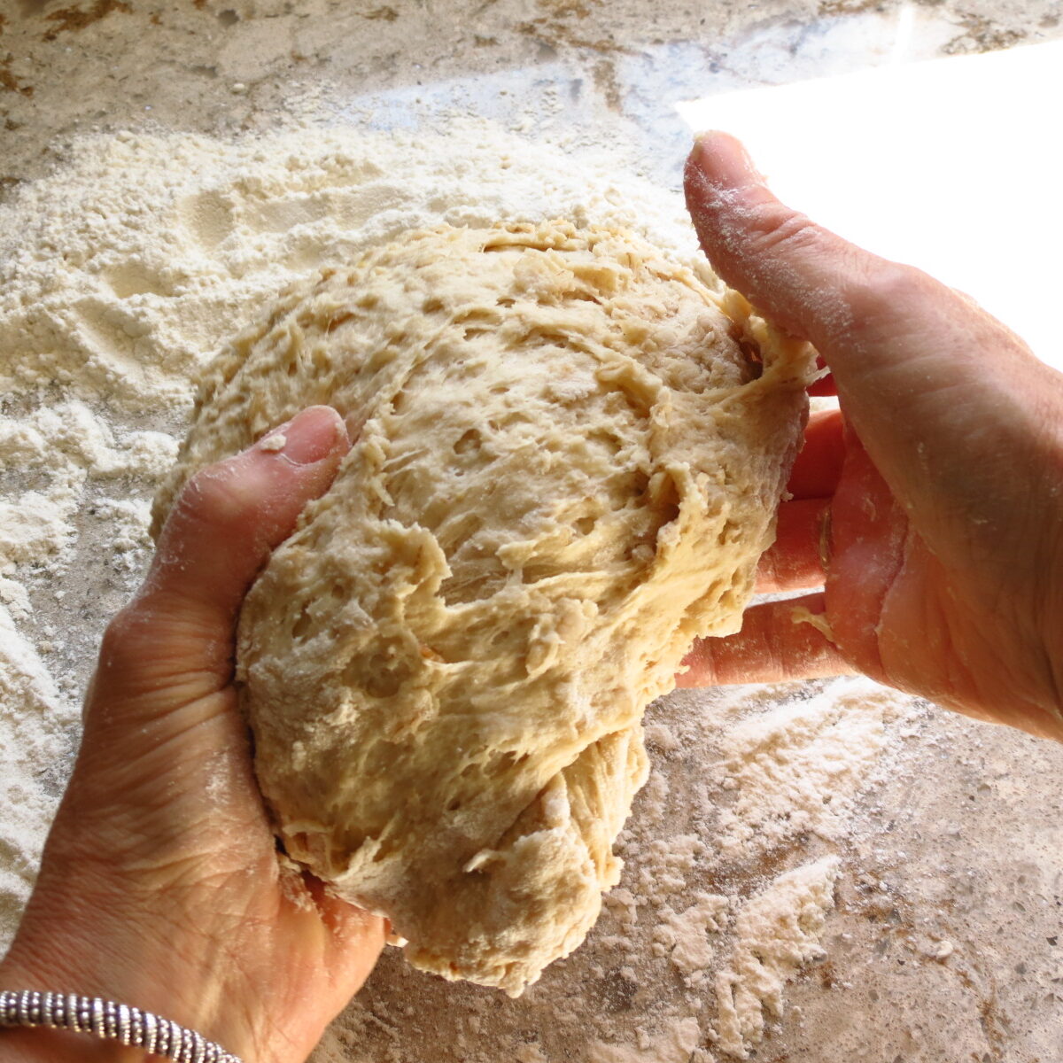 Two hands handling bread dough over a floured surface.