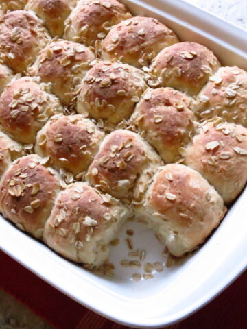 A white, rectangle pan of oatmeal rolls.