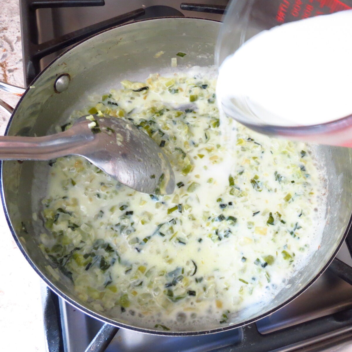 Milk poured into a skillet of cooked onion and peppers.