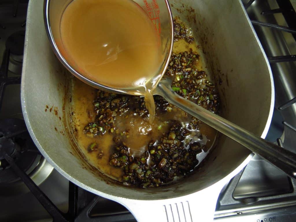 Rich stock poured into a large pot of dark roux.