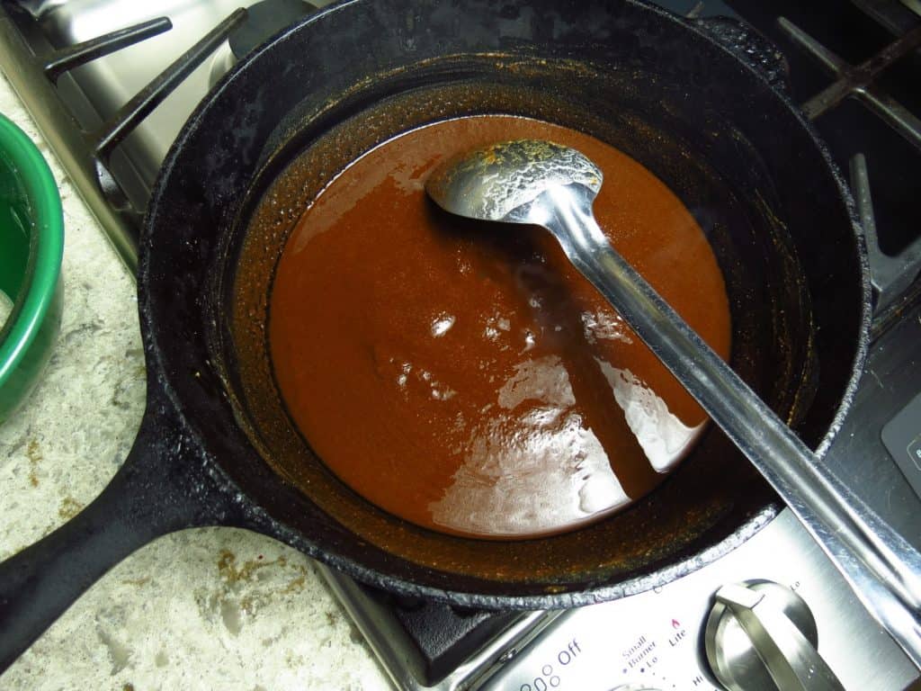 A black pot of dark roux on the stove with a silver spoon.
