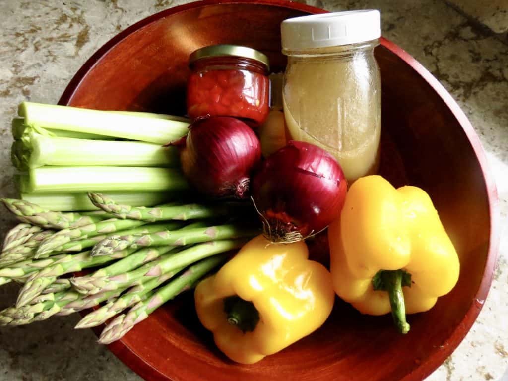 Fresh vegetables in a wooden bowl with a jar of salad dressing.