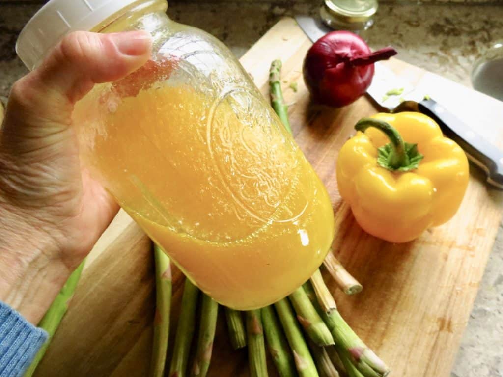 A jar of marinating salad dressing with vegetables.