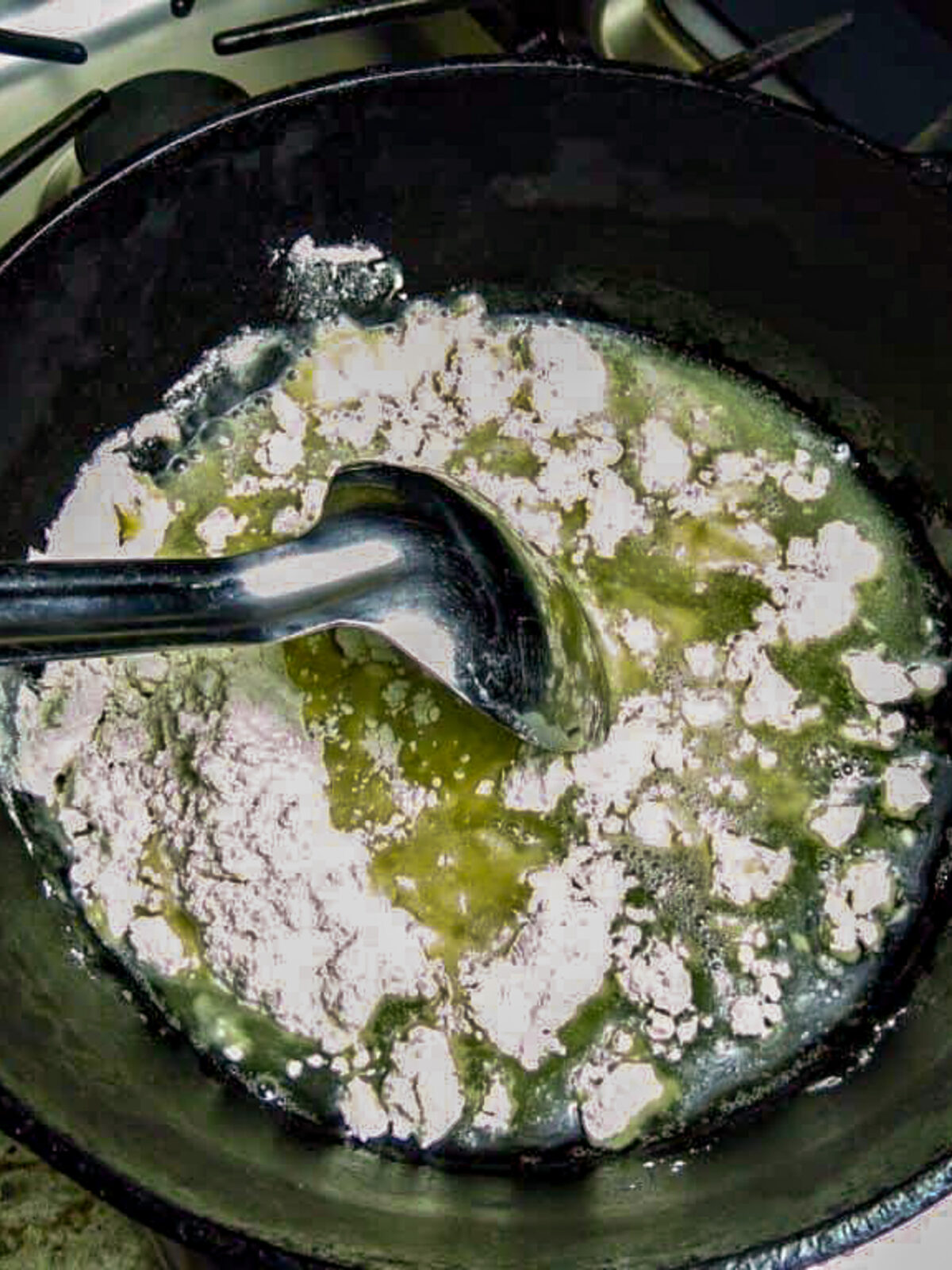 Flour and oil stiired in a black pot by a silver spoon for a roux.