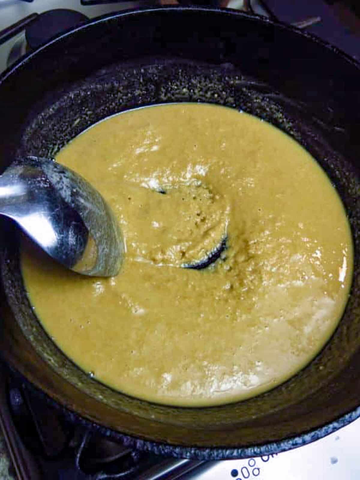 A silver spoon stirring a blonde colored roux in a black pot for a Cajun Roux recipe.